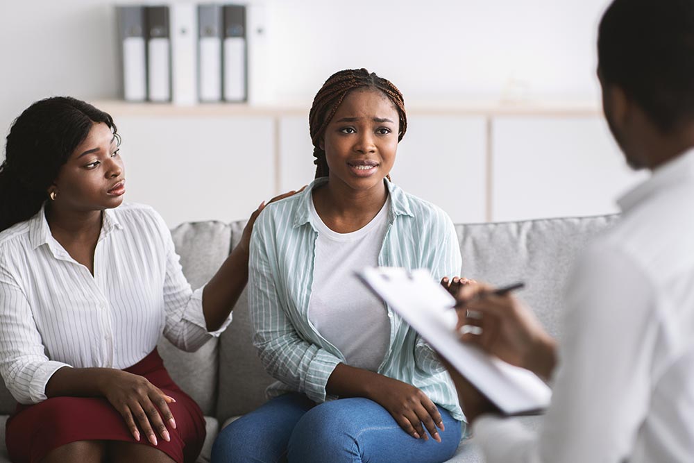 A woman sits on a couch next to a family member as a doctor talks to them about organ donation.